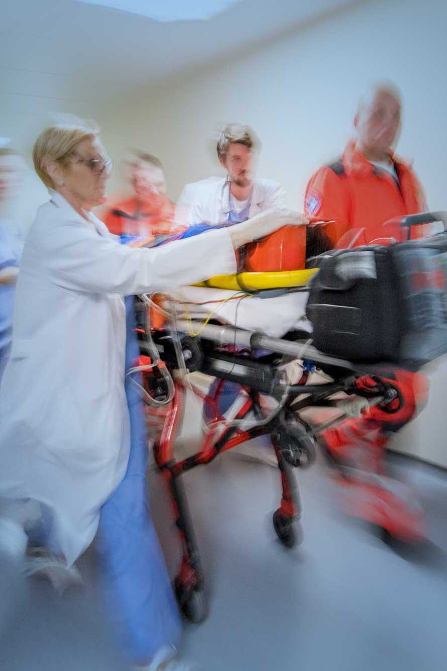 Paramedics, doctor and nurse wheeling patient on stretcher in hospital corridor.