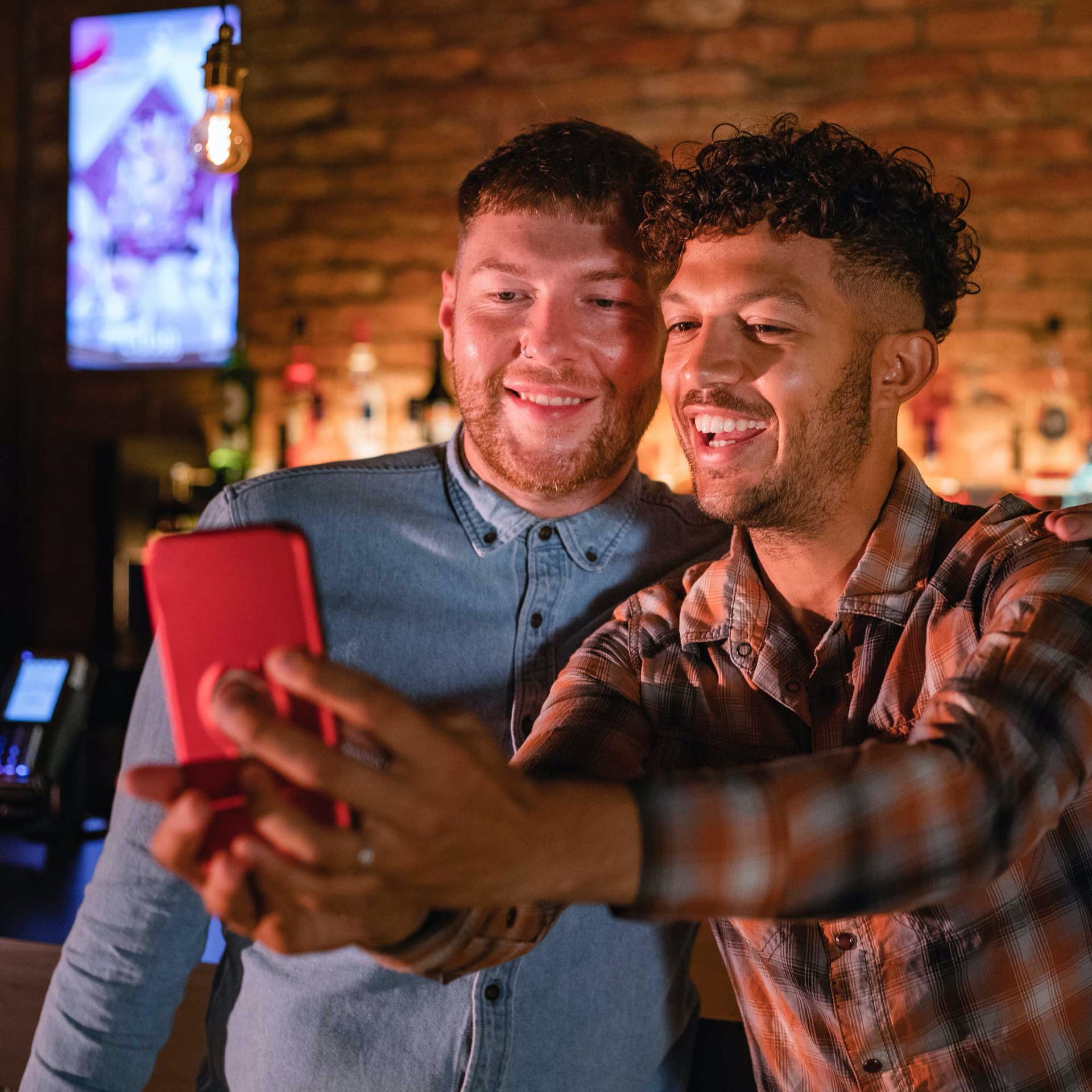 Gay couple taking a selfie in a bar.