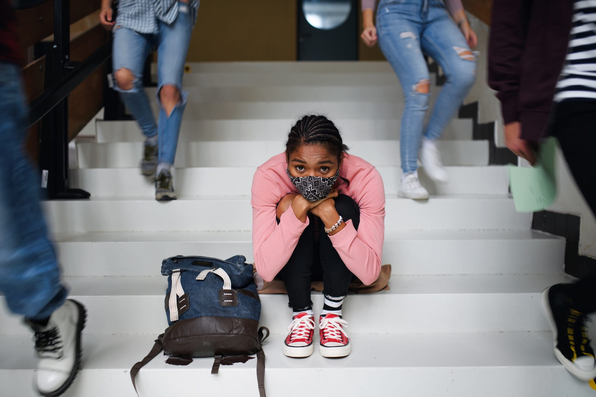 Student sitting on school steps with a mask on.